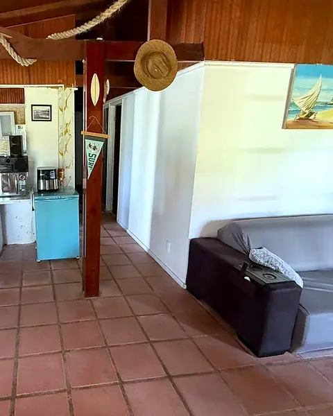 Sala com sofá e teto de madeira, com a cozinha ao fundo