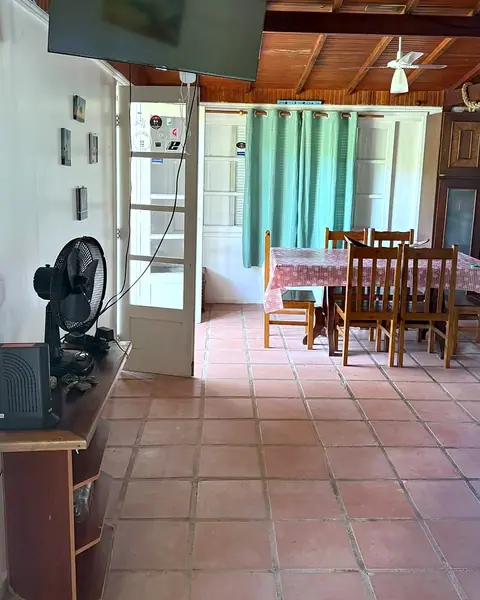 Sala com TV e ventilador, com a mesa de jantar ao fundo