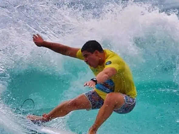 Surfista de lycra amarela fazendo uma manobra numa onda verde-água