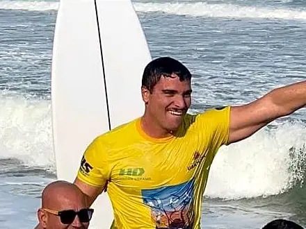 Gabriel, de lycra amarela, carregado nos ombros na beira do mar em Itamambuca